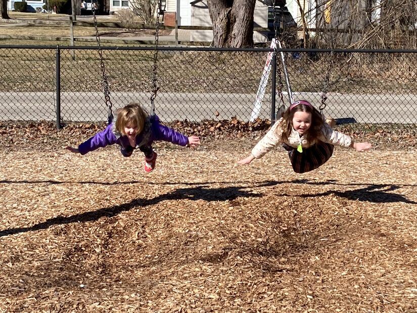 Two elementary students on playground swings with their arms outstretched